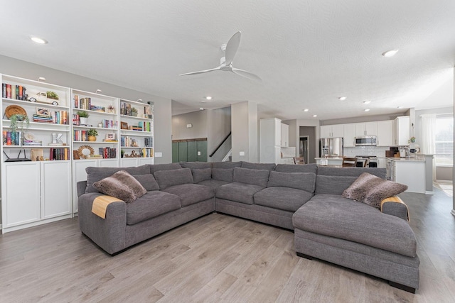 living room with ceiling fan, a textured ceiling, and light wood-type flooring