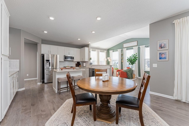 dining space with vaulted ceiling, a textured ceiling, and light hardwood / wood-style flooring