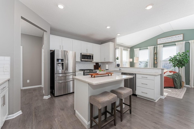 kitchen featuring white cabinetry, a kitchen breakfast bar, a kitchen island, stainless steel appliances, and backsplash