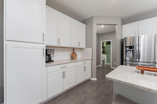 kitchen featuring stainless steel refrigerator with ice dispenser, white cabinetry, tasteful backsplash, and light stone counters