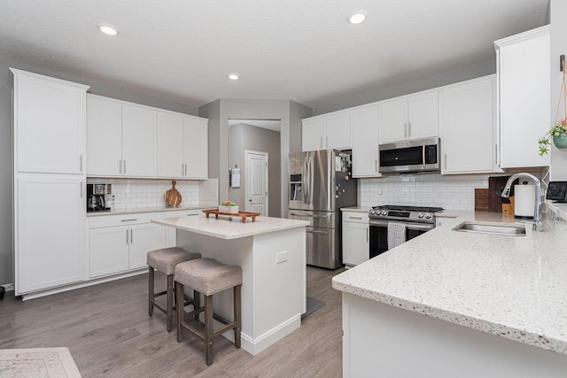 kitchen featuring a kitchen bar, sink, appliances with stainless steel finishes, a kitchen island, and white cabinets