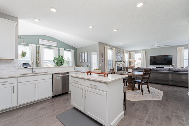 kitchen featuring lofted ceiling, sink, dishwasher, light stone countertops, and white cabinets