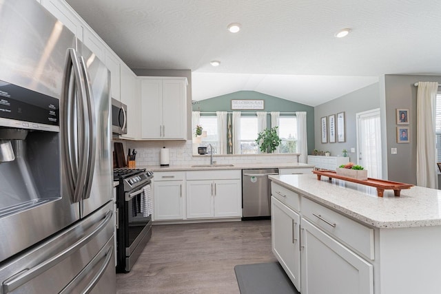 kitchen featuring sink, appliances with stainless steel finishes, light stone countertops, white cabinets, and vaulted ceiling