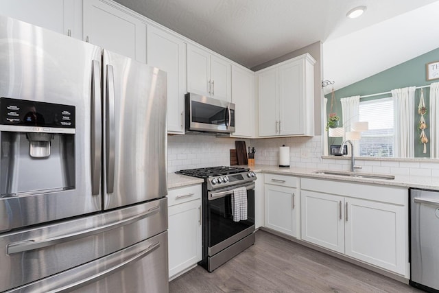 kitchen featuring sink, appliances with stainless steel finishes, tasteful backsplash, light stone countertops, and white cabinets