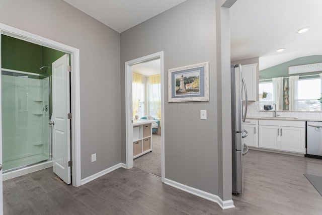 bathroom with a shower with shower door, wood-type flooring, lofted ceiling, backsplash, and vanity