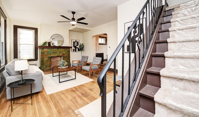 living room with a tile fireplace, wood-type flooring, and ceiling fan