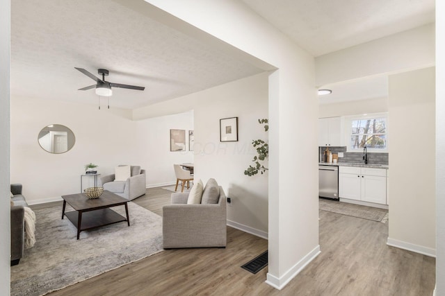 living room featuring ceiling fan, sink, a textured ceiling, and light wood-type flooring