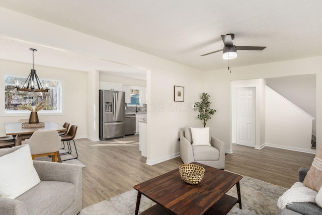 living room featuring sink, ceiling fan with notable chandelier, and light wood-type flooring