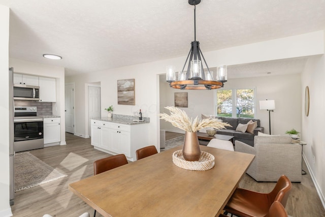 dining area with light hardwood / wood-style floors, a textured ceiling, and a notable chandelier