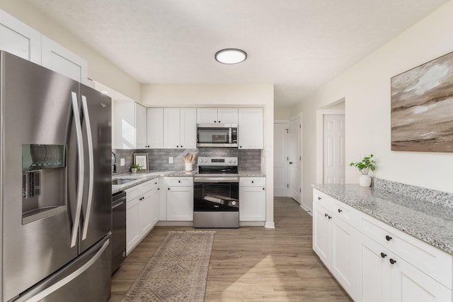 kitchen featuring appliances with stainless steel finishes, white cabinetry, backsplash, light stone counters, and light hardwood / wood-style floors