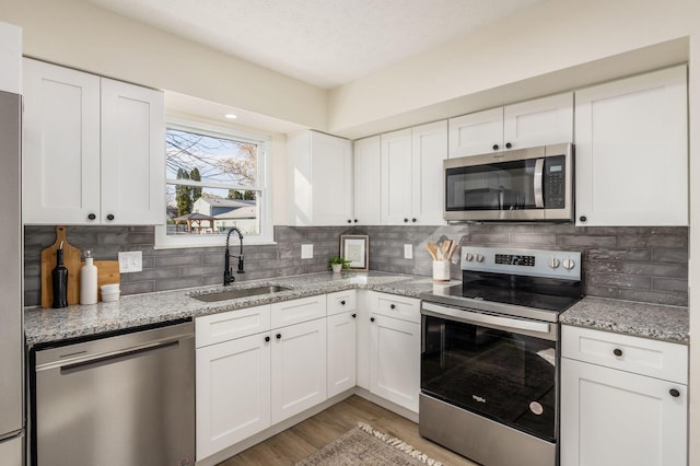 kitchen featuring white cabinetry, sink, stainless steel appliances, and light stone countertops