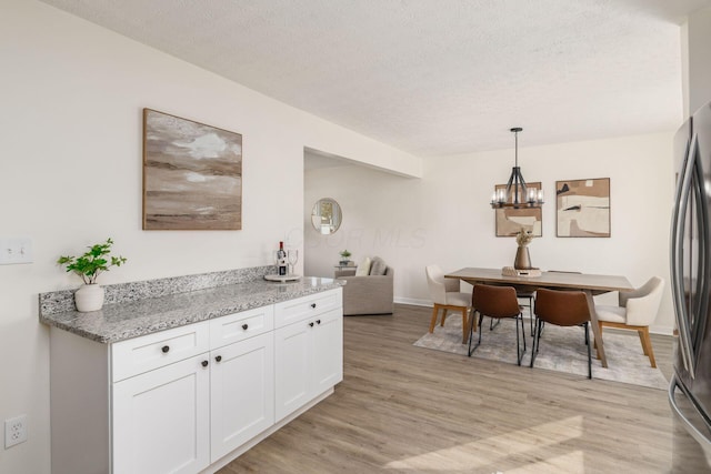 kitchen featuring white cabinetry, light stone counters, hanging light fixtures, light wood-type flooring, and stainless steel refrigerator