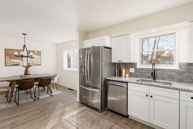 kitchen with sink, white cabinetry, light stone counters, hanging light fixtures, and appliances with stainless steel finishes