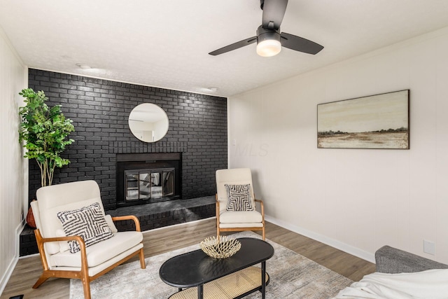 sitting room featuring hardwood / wood-style flooring, a brick fireplace, and ceiling fan