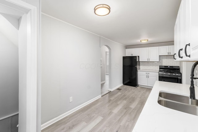 kitchen featuring white cabinetry, decorative backsplash, black fridge, light stone countertops, and stainless steel range with gas stovetop