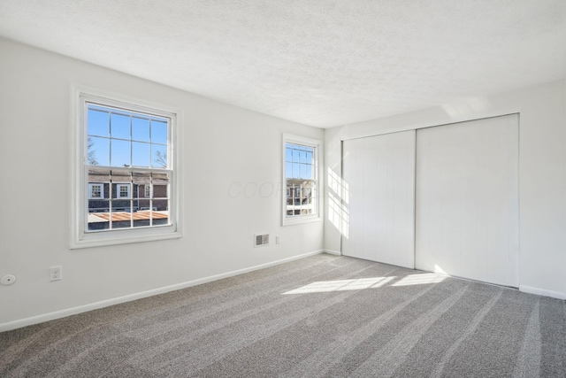 unfurnished bedroom featuring a closet, carpet, baseboards, visible vents, and a textured ceiling