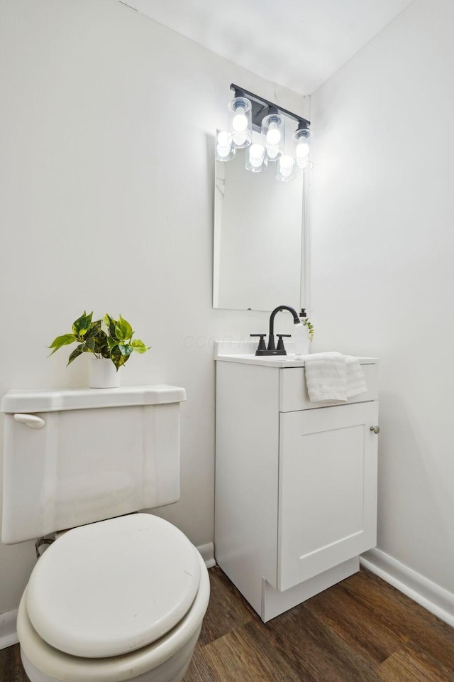 half bath featuring toilet, baseboards, wood finished floors, and vanity