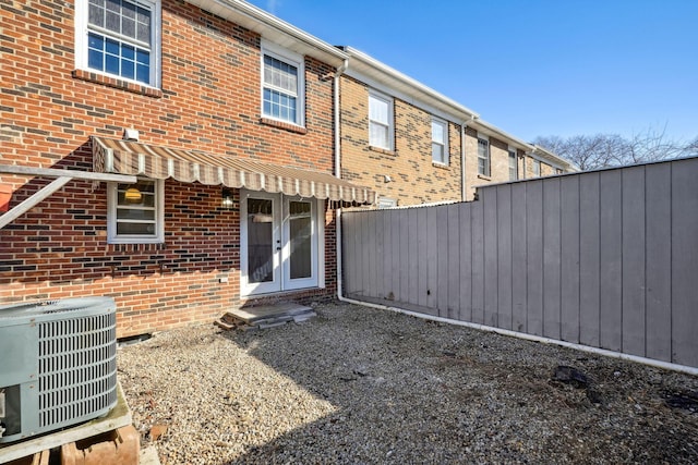 rear view of house with central AC, french doors, fence, and brick siding