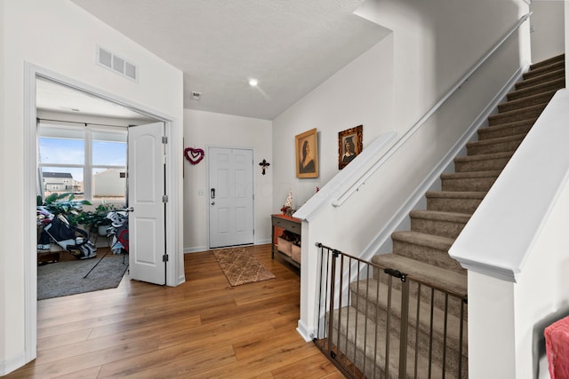 entryway featuring baseboards, wood finished floors, visible vents, a textured ceiling, and stairway