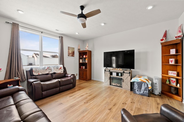 living room with a glass covered fireplace, light wood-type flooring, visible vents, recessed lighting, and a ceiling fan