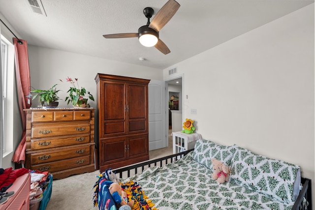 carpeted bedroom featuring a textured ceiling, visible vents, and ceiling fan