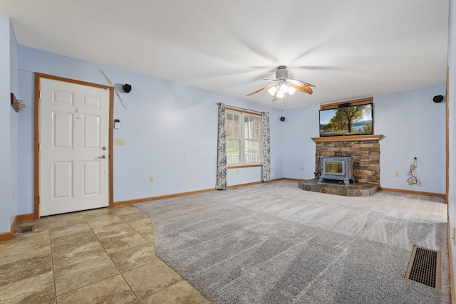 unfurnished living room featuring carpet, a wood stove, and ceiling fan