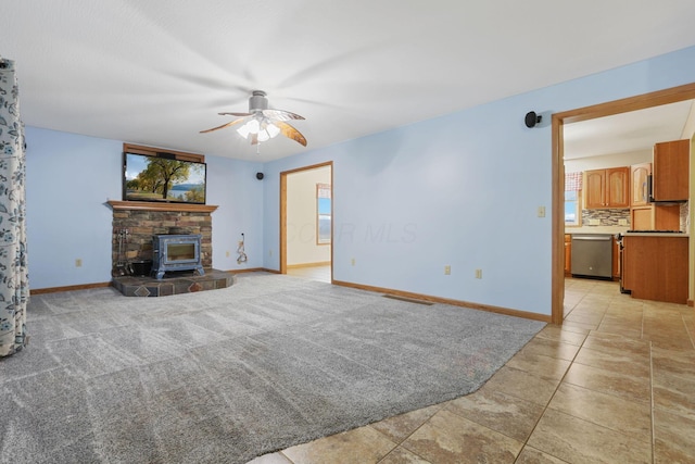 unfurnished living room featuring ceiling fan, light colored carpet, and a wood stove