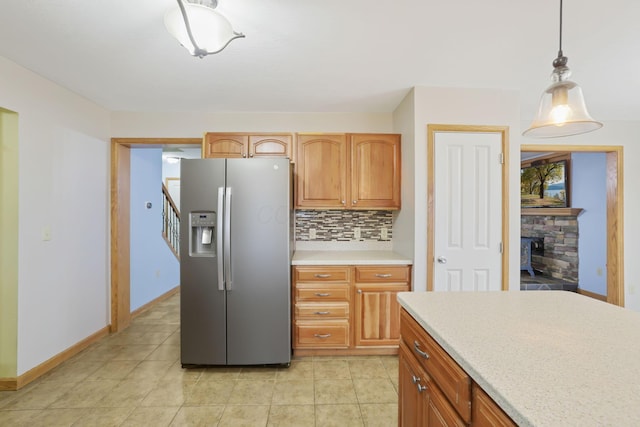 kitchen with light tile patterned floors, stainless steel fridge, hanging light fixtures, tasteful backsplash, and a fireplace