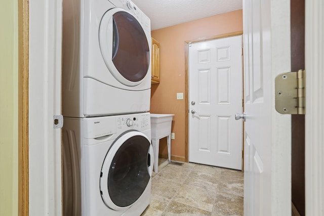 clothes washing area with cabinets, stacked washer and clothes dryer, and a textured ceiling