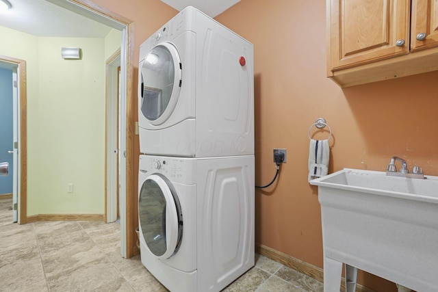 clothes washing area with stacked washer and dryer, sink, and cabinets