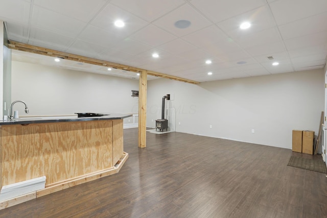 bar with a drop ceiling, sink, dark wood-type flooring, and a wood stove