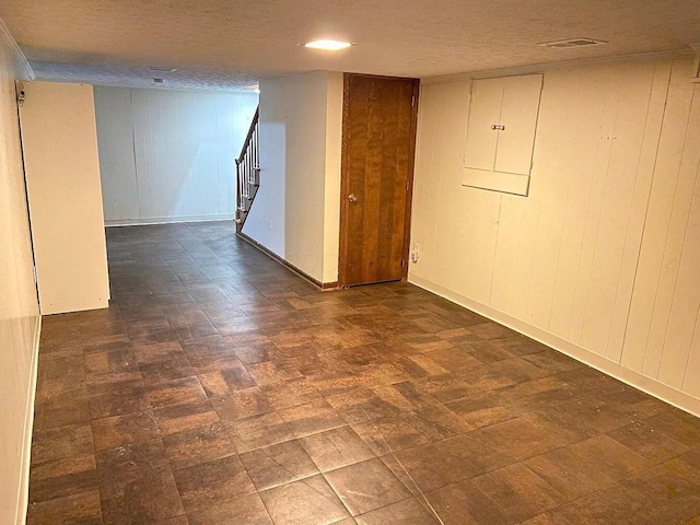 basement featuring wooden walls, electric panel, and a textured ceiling