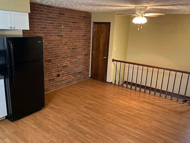 interior space with brick wall, black refrigerator, white cabinets, and light hardwood / wood-style floors