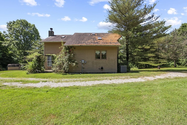 rear view of house featuring a chimney, central AC, and a yard