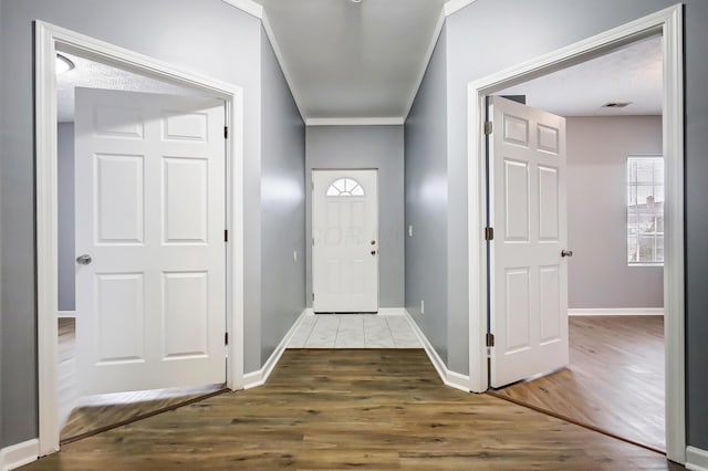 foyer entrance featuring crown molding, wood finished floors, baseboards, and visible vents