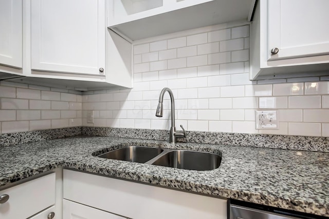 kitchen featuring dark stone counters, white cabinets, backsplash, and a sink