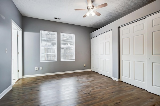 unfurnished bedroom featuring visible vents, a textured ceiling, dark wood-type flooring, and multiple closets