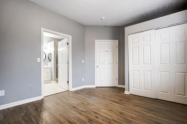 unfurnished bedroom with baseboards, ensuite bathroom, wood finished floors, a closet, and a textured ceiling