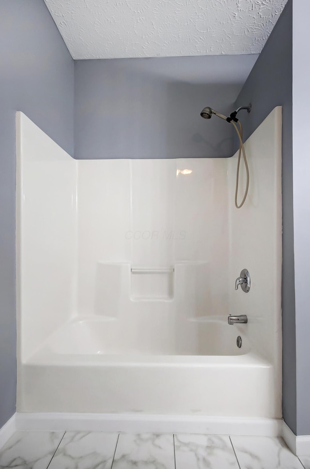 bathroom featuring marble finish floor, a textured ceiling, baseboards, and washtub / shower combination