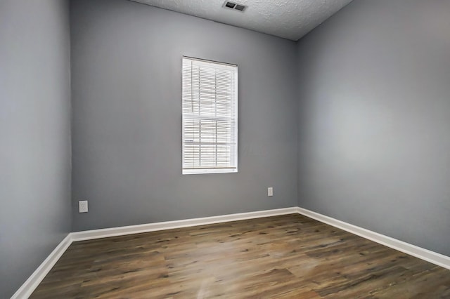 unfurnished room with baseboards, wood finished floors, visible vents, and a textured ceiling