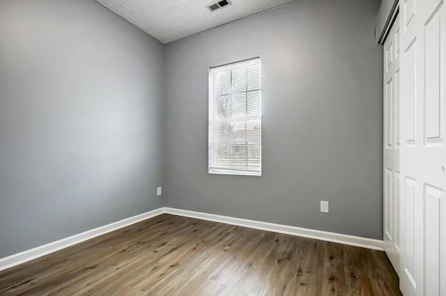 unfurnished bedroom with visible vents, a textured ceiling, wood finished floors, a closet, and baseboards