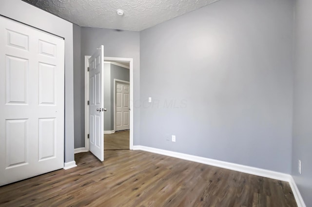 unfurnished bedroom with a closet, a textured ceiling, baseboards, and wood finished floors