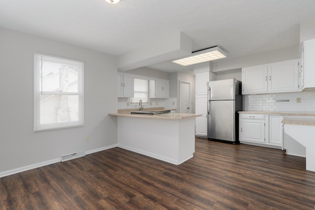 kitchen with a peninsula, visible vents, light countertops, freestanding refrigerator, and dark wood finished floors