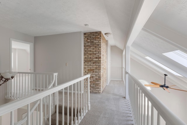 hall featuring a textured ceiling, carpet floors, lofted ceiling with skylight, and an upstairs landing