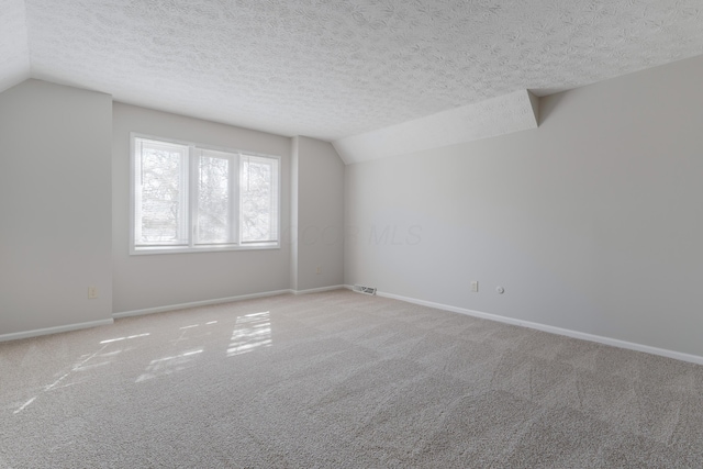 unfurnished room featuring lofted ceiling, light colored carpet, visible vents, and a textured ceiling