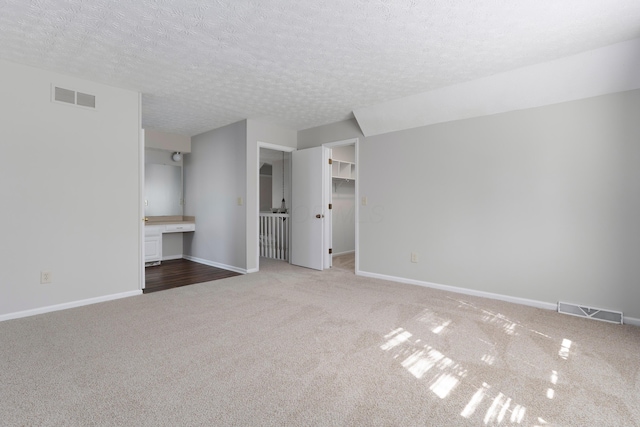 unfurnished living room featuring a textured ceiling, carpet floors, visible vents, and baseboards