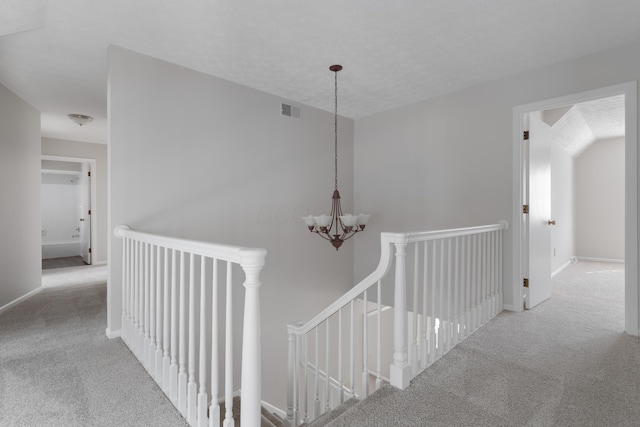 hall with carpet, visible vents, a notable chandelier, and an upstairs landing