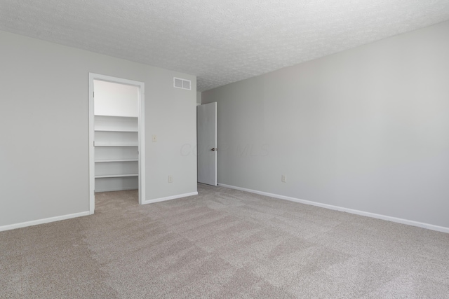 unfurnished bedroom with a textured ceiling, a spacious closet, visible vents, and baseboards