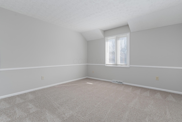 spare room with carpet floors, visible vents, vaulted ceiling, a textured ceiling, and baseboards