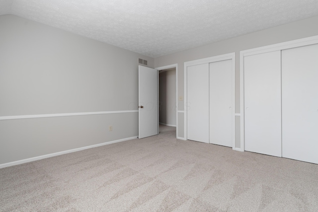 unfurnished bedroom featuring a textured ceiling, lofted ceiling, carpet floors, visible vents, and two closets